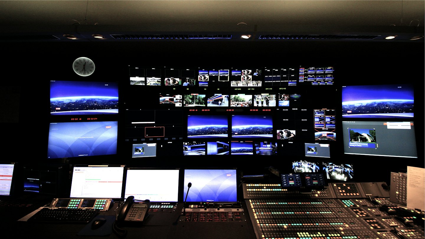Broadcast control room with glowing monitors and control panels.