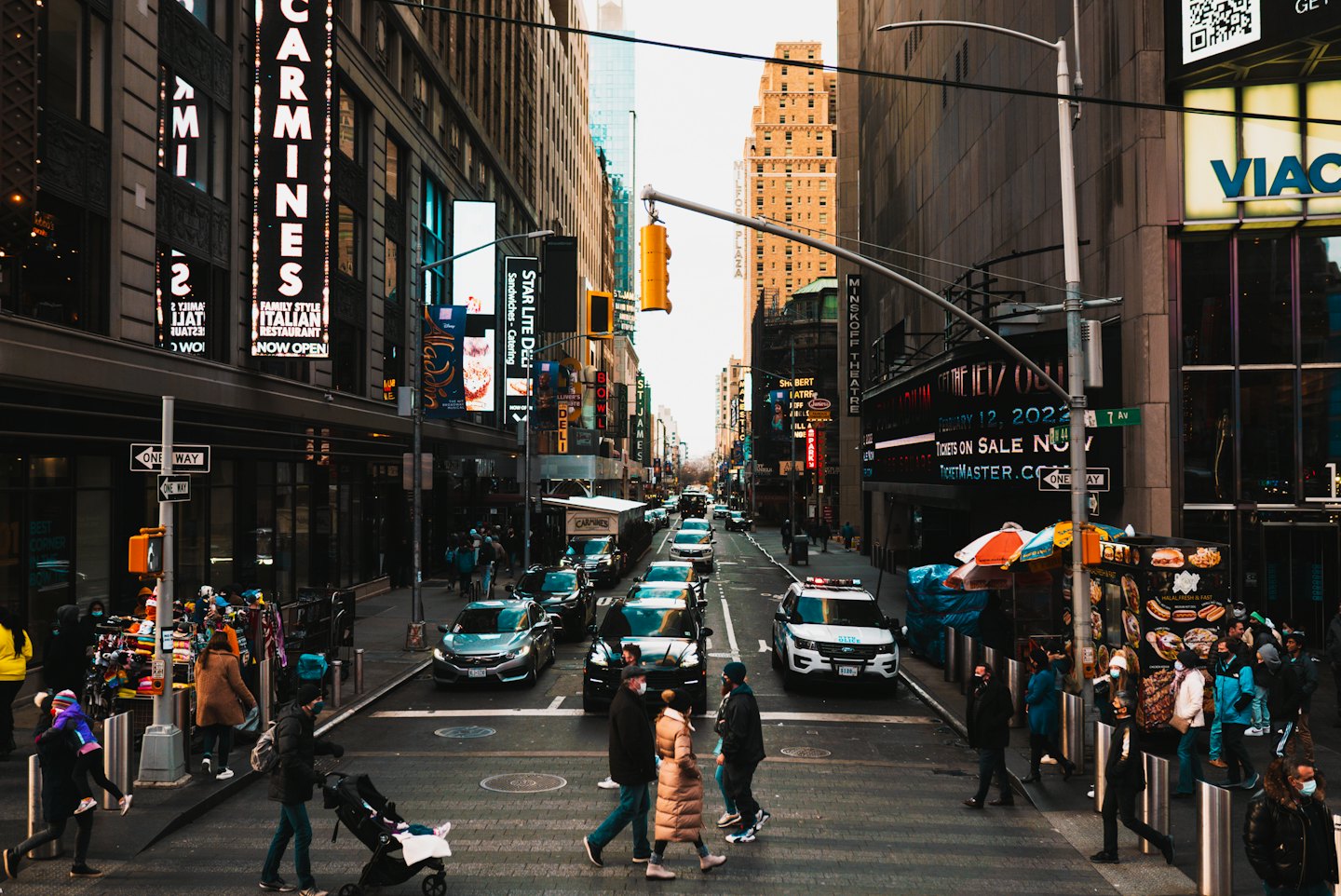 Pedestrians walk on a busy city street lined with buildings.