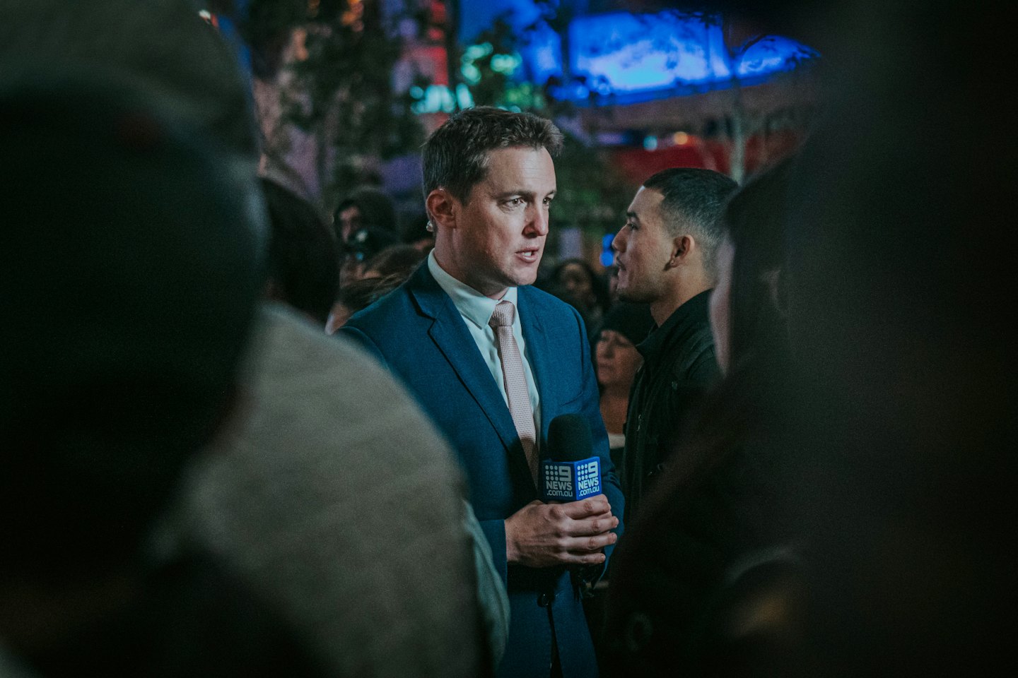 Reporter in a blue suit interviews a man outdoors at night.